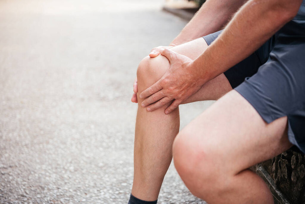 Ένας άντρας που κάνει μασάζ στα γόνατα ενώ υποφέρει από πόνο στις αρθρώσεις των αδένων. - Φωτογραφία, εικόνα