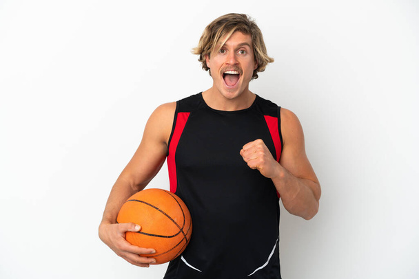 Young blonde man holding a ball of basketball isolated on white background celebrating a victory in winner position - Photo, Image