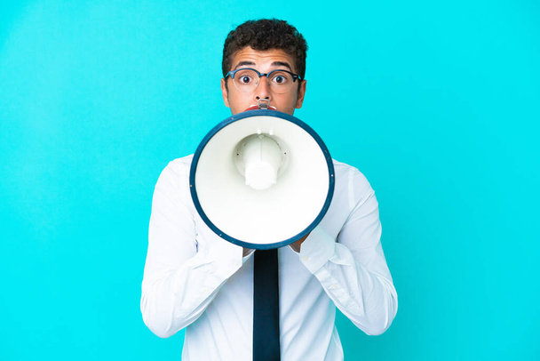 Young business Brazilian man isolated on blue background shouting through a megaphone - Foto, imagen