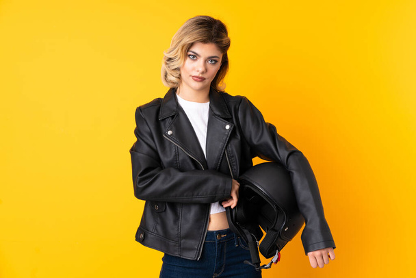 Teenager woman holding a motorcycle helmet isolated on yellow background keeping arms crossed - Zdjęcie, obraz
