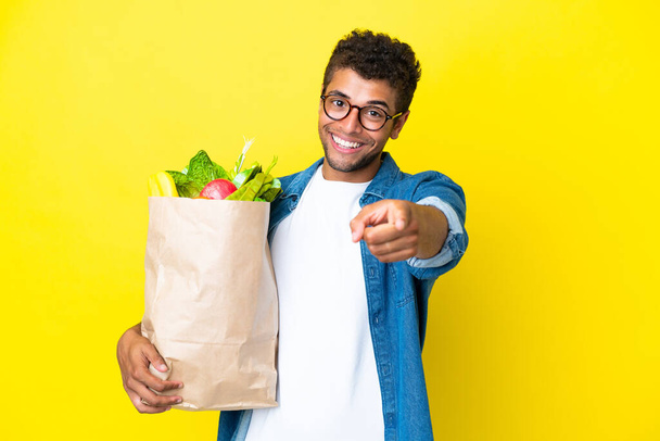 Junger brasilianischer Mann mit einer Einkaufstasche auf gelbem Hintergrund und fröhlichem Gesichtsausdruck - Foto, Bild
