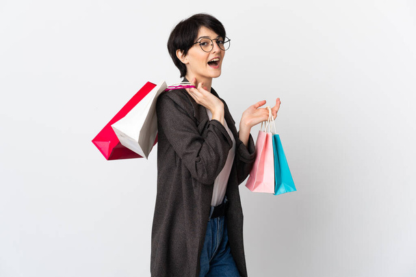Frau mit kurzen Haaren auf weißem Hintergrund hält Einkaufstüten und lächelt - Foto, Bild