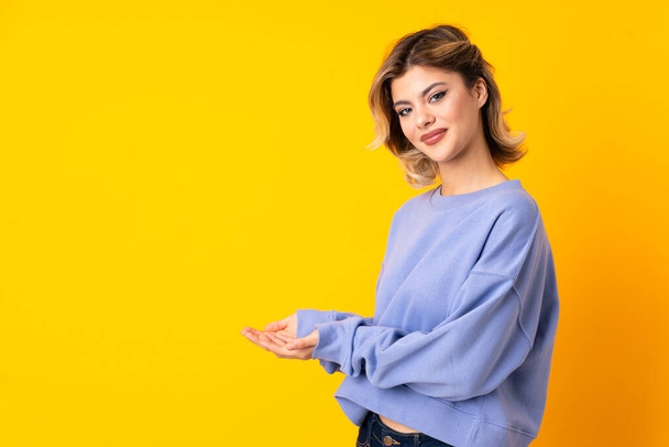 Young Russian woman isolated on yellow background extending hands to the side for inviting to come - Φωτογραφία, εικόνα