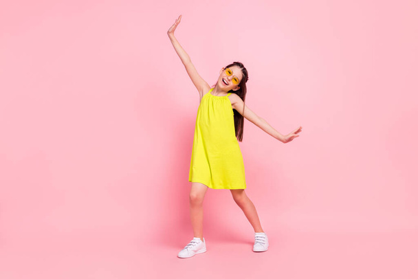 Full length photo of funny adorable schoolgirl dressed yellow dress glasses dancing smiling arms sides isolated pink color background - Photo, Image