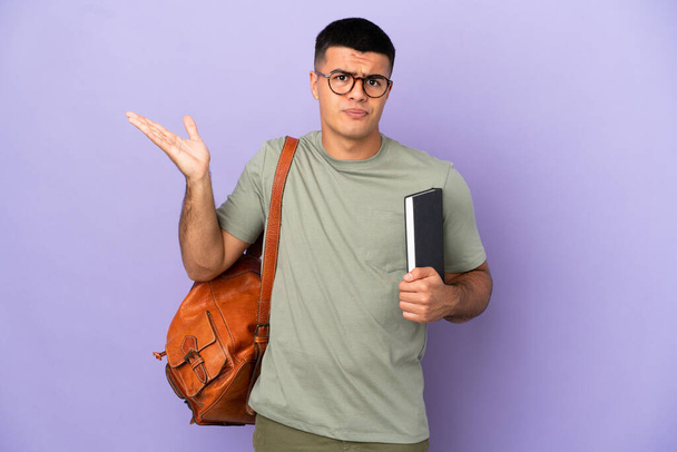 Handsome student man over isolated background having doubts while raising hands - Фото, изображение