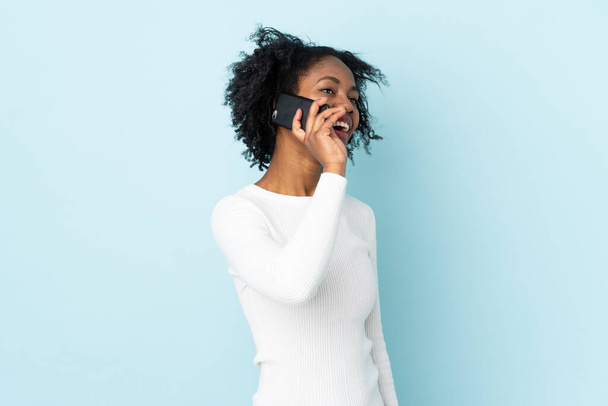 Young African American woman isolated on blue background keeping a conversation with the mobile phone - Foto, afbeelding