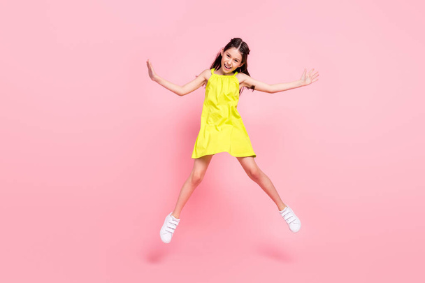 Foto de cuerpo entero de adorable bonita colegiala vestida con traje amarillo gafas oscuras saltando alto sonriente aislado color rosa fondo - Foto, imagen