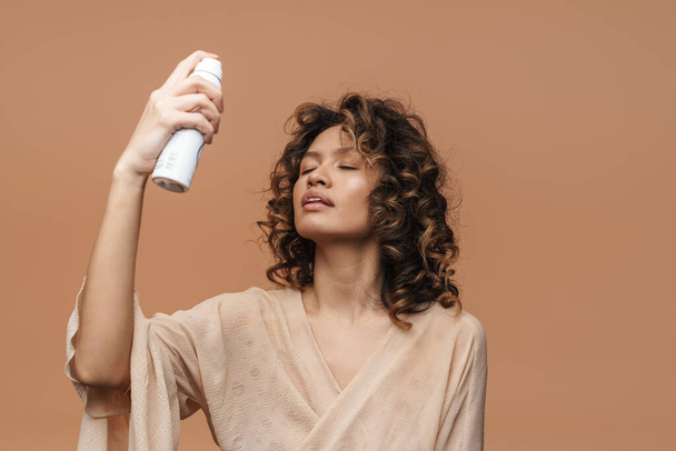 Young hispanic woman applying beauty product on her face isolated over beige background - Foto, afbeelding