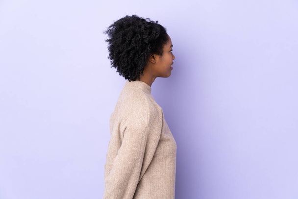 Νεαρή Αφροαμερικανή γυναίκα απομονωμένη σε μωβ φόντο στην πίσω θέση και κοιτάζοντας πίσω - Φωτογραφία, εικόνα