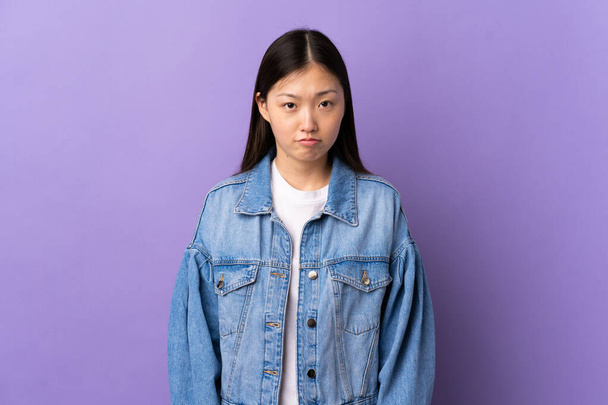 jong Chinees meisje over geïsoleerde paarse achtergrond met droevige uitdrukking - Foto, afbeelding