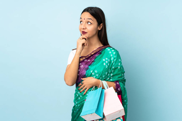 Alışveriş torbaları taşıyan genç Hintli kadın yukarı bakarken bir fikir düşünüyor. - Fotoğraf, Görsel