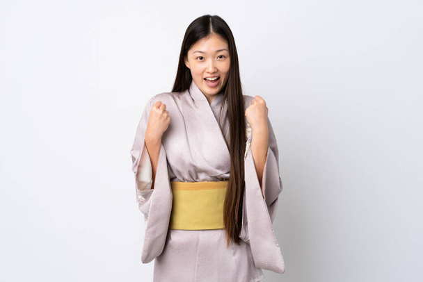 Joven chica china usando kimono sobre fondo aislado celebrando una victoria en posición ganadora - Foto, Imagen