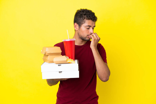 Elinde pizza ve hamburger tutan Brezilyalı genç bir adam şüpheli bir şekilde izole edilmiş. - Fotoğraf, Görsel