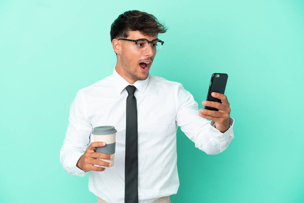 Επιχειρηματίας καυκάσιος άνθρωπος απομονωμένος σε μπλε φόντο κρατώντας καφέ για να πάρει μακριά και ένα κινητό - Φωτογραφία, εικόνα