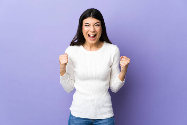 Young brunette woman over isolated purple background celebrating a victory in winner position - Photo, image