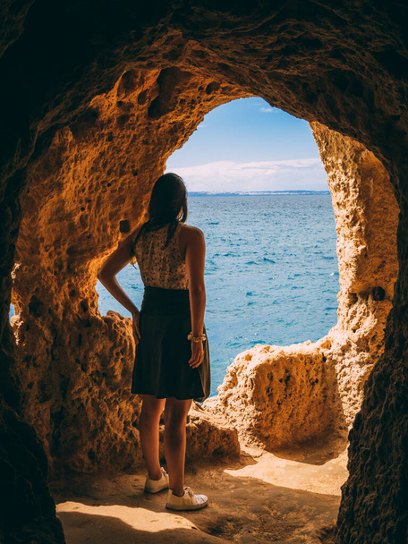 A vertical shot of the girl in the cave with Algar Seco near Carvoeiro in Algarve, Portugal. - 写真・画像