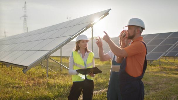 Három napenergia specialista egy naperőműben. Professzionális mérnökök megvitatják az innovatív projektet. Ipari technikusok csapata a napparkban. Naperőmű építése. - Fotó, kép