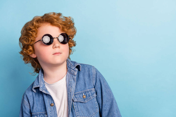 Foto retrato rizado niño buscando espacio en blanco usando gafas de sol de moda aislado pastel fondo de color azul - Foto, Imagen