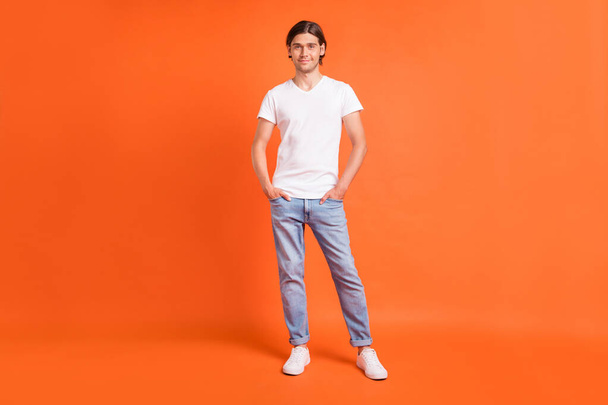 Full body photo of young positive charming attractive man smile hold hands pockets isolated on orange color background - Фото, зображення
