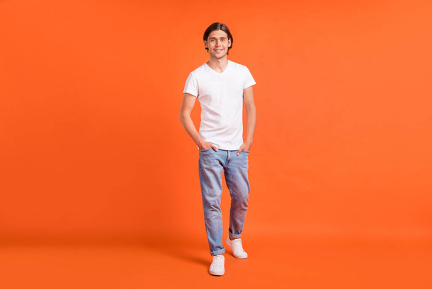 Full body photo of young happy man walk hands pockets jeans isolated on shine orange color background - Photo, image