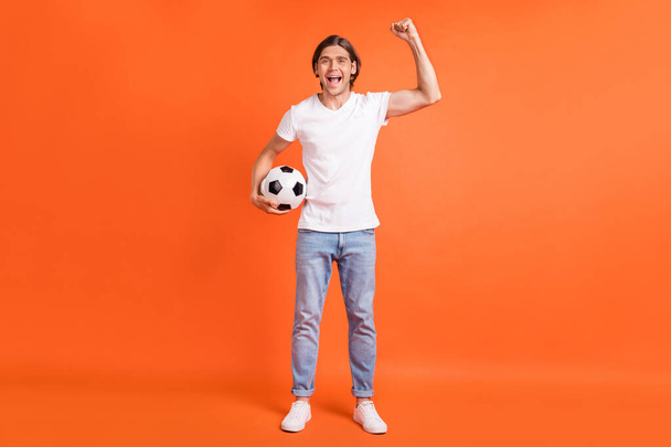 Full body photo of young cheerful happy man raise hand winner football isolated on orange color background - 写真・画像