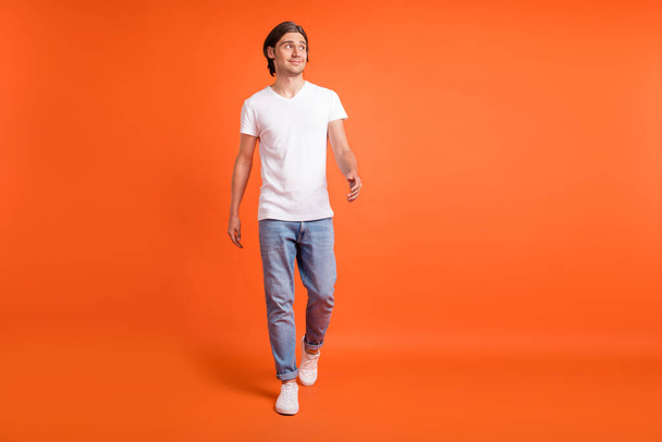 Full size photo of happy positive cheerful man look empty space walk good mood isolated on orange color background - Fotoğraf, Görsel