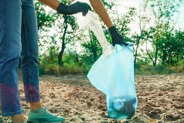 Woman puts a plastic bottle in a trash bag. Garbage collection in the nature. - 写真・画像