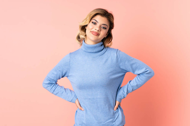 Young Russian woman isolated on pink background posing with arms at hip and smiling - Photo, Image