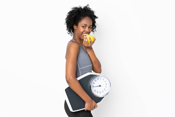 Young African American woman isolated on white background with weighing machine and with an apple - Foto, Imagen