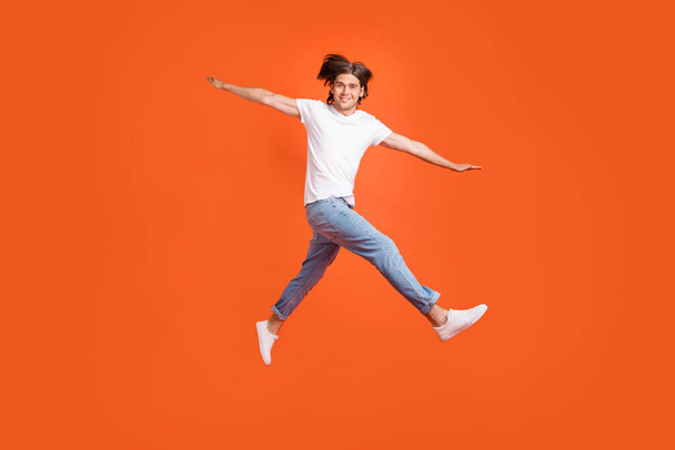 Full body photo of cheerful young happy positive man jump up hands plane wings isolated on orange color background - Photo, Image