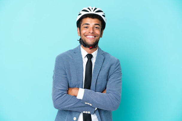 Junger Geschäftsmann brasilianischer Abstammung mit Fahrradhelm auf blauem Hintergrund, der die Arme frontal gekreuzt hält - Foto, Bild