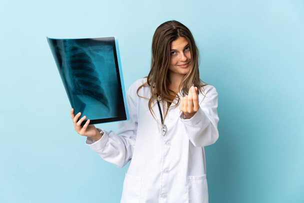 Young doctor woman holding radiography over isolated background making money gesture - Foto, Imagem
