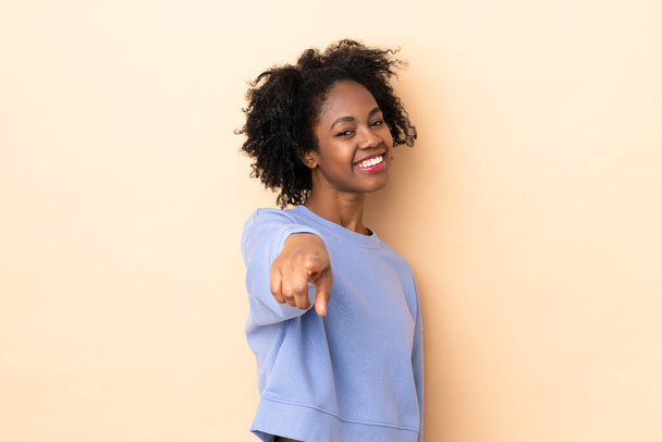 Jeune femme afro-américaine isolée sur fond beige pointant devant avec expression heureuse - Photo, image