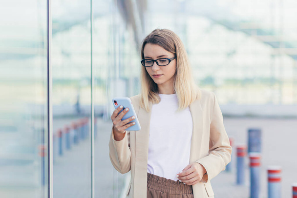 portrait of a serious business woman with glasses blonde reads the news from a mobile phone uses the application to rewrite messages - 写真・画像