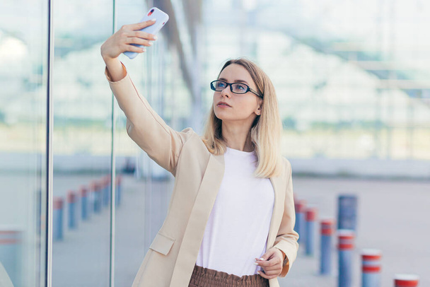 woman wearing glasses blonde holding a mobile phone takes a selfie photo - Zdjęcie, obraz