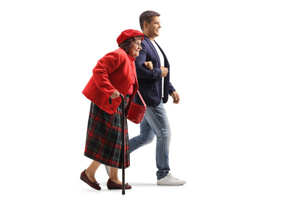 Full length profile shot of a young man helping an elderly woman walking isolated on white background - Photo, Image