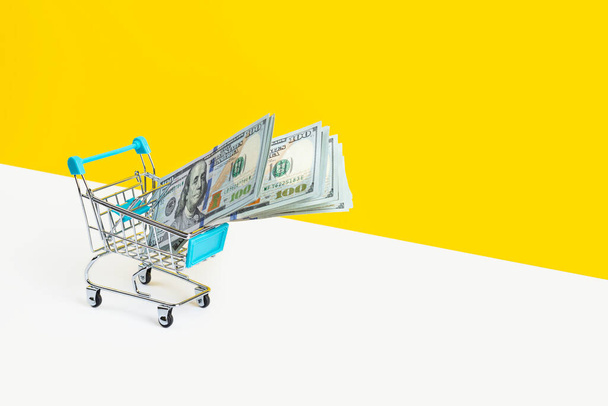 Іграшковий кошик для супермаркетів або візок для покупок, повний грошей, ізольовані на жовтому тлі. Концепція грошового кредиту або продажу. Прапор з пробілом для копіювання
 - Фото, зображення