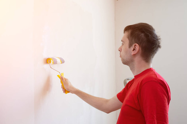 Man priming the wall with a roller. Repair of the interior. Young male decorator painting a wall in the empty room. Concept renovation do it yourself - Фото, зображення