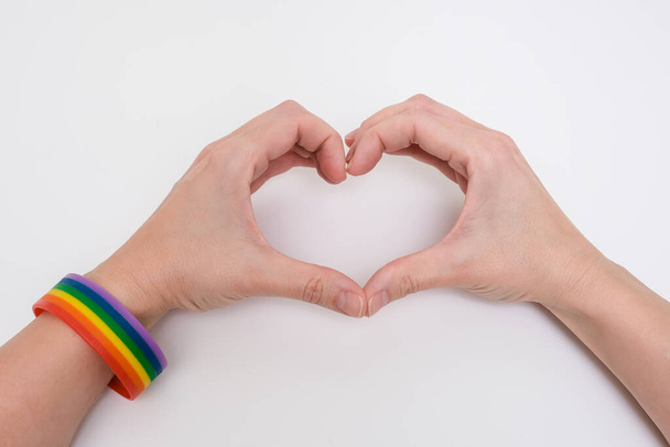 Hands wearing lgbtq rainbow bracelet folding a shape of a heart - Foto, imagen