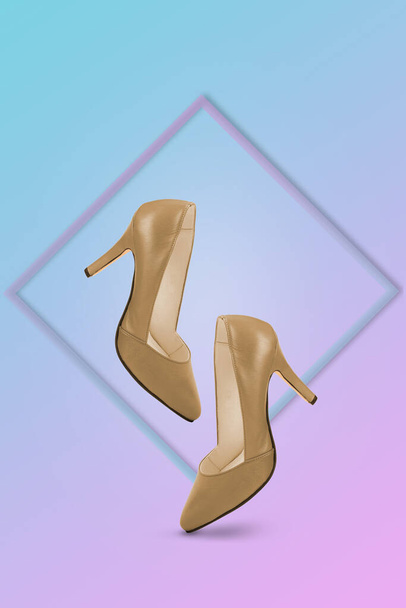 Gouden hoge hakken op een trendy achtergrond verlicht door een blauw en roze kleurverloop met een frame. Creatief minimaal concept van vrouwelijkheid, trend en mode. Kopieerruimte. - Foto, afbeelding