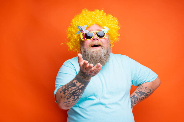 Товстий щасливий чоловік з бородою, татуюваннями та сонцезахисними окулярами розважається з жовтим перцем
 - Фото, зображення