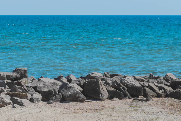 Παραλία Breakwater πέτρες στην ακτή της θάλασσας με μπλε νερά στο φόντο της γραμμής του ορίζοντα. - Φωτογραφία, εικόνα