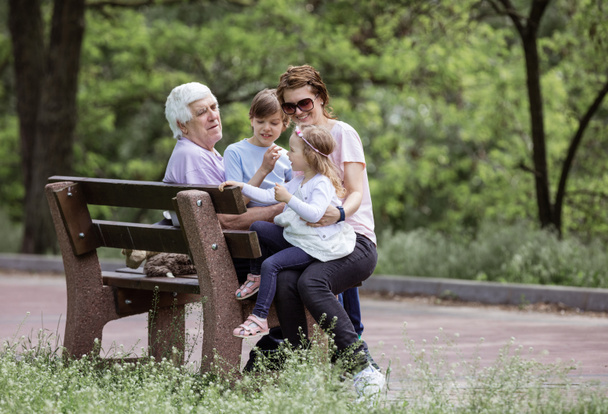 Třígenerační rodina odpočívající na lavičce v letním parku: dědeček, matka a vnoučata - Fotografie, Obrázek
