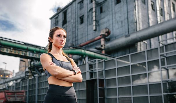 Sportswoman with crossed arms posing in front of a factory - Fotografie, Obrázek