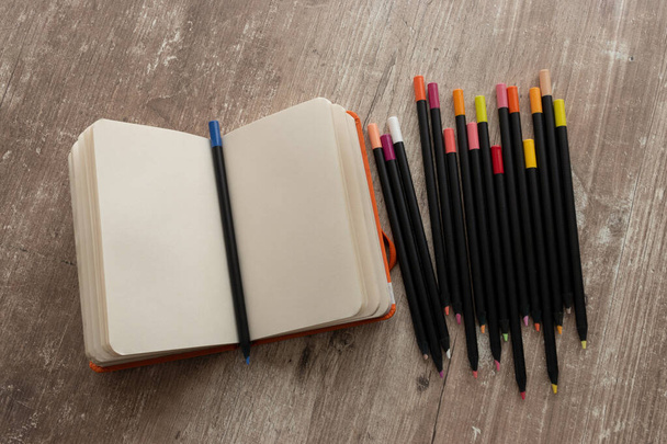 detalhe de notebook com folhas em branco e lápis de cor, em uma mesa de madeira texturizada, instrumentos de escritório no espaço de trabalho, detalhe de objetos artísticos em estúdio - Foto, Imagem