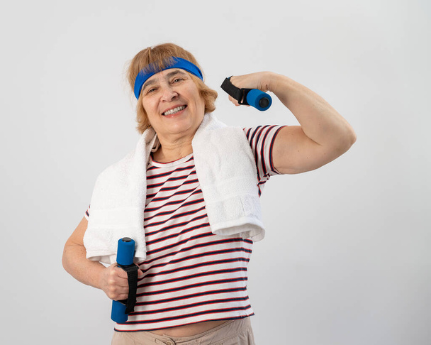 An elderly woman with a blue bandage on her head trains with dumbbells on a white background - Фото, зображення