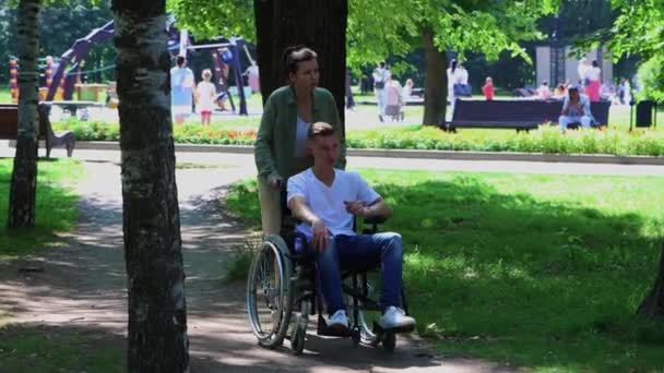 A woman walking with a guy in a wheelchair in the park - Footage, Video