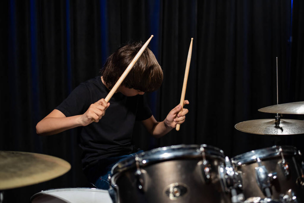 The boy learns to play the drums in the studio on a black background. Music school student - Valokuva, kuva