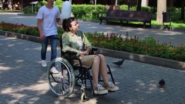 Скучная женщина в инвалидной коляске сидит в парке - ее парень приходит к ней со спины и приносит ей сахарной ваты - Кадры, видео