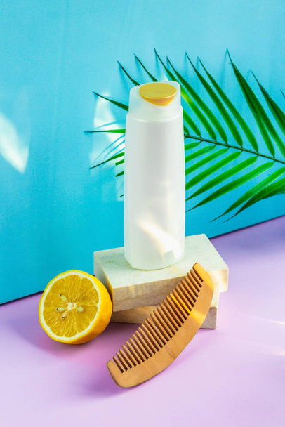 Hair cosmetics on a blue-purple background. an organic moisturizing shampoo sits on a granite slab podium, a comb with wide teeth for styling, and half a yellow lemon lies next to it. - Фото, зображення
